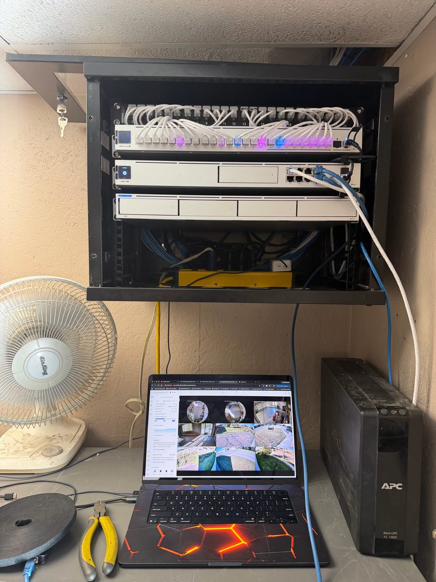 Wall rack with UniFi gateway, NVR, and switch beside a laptop showing the camera grid