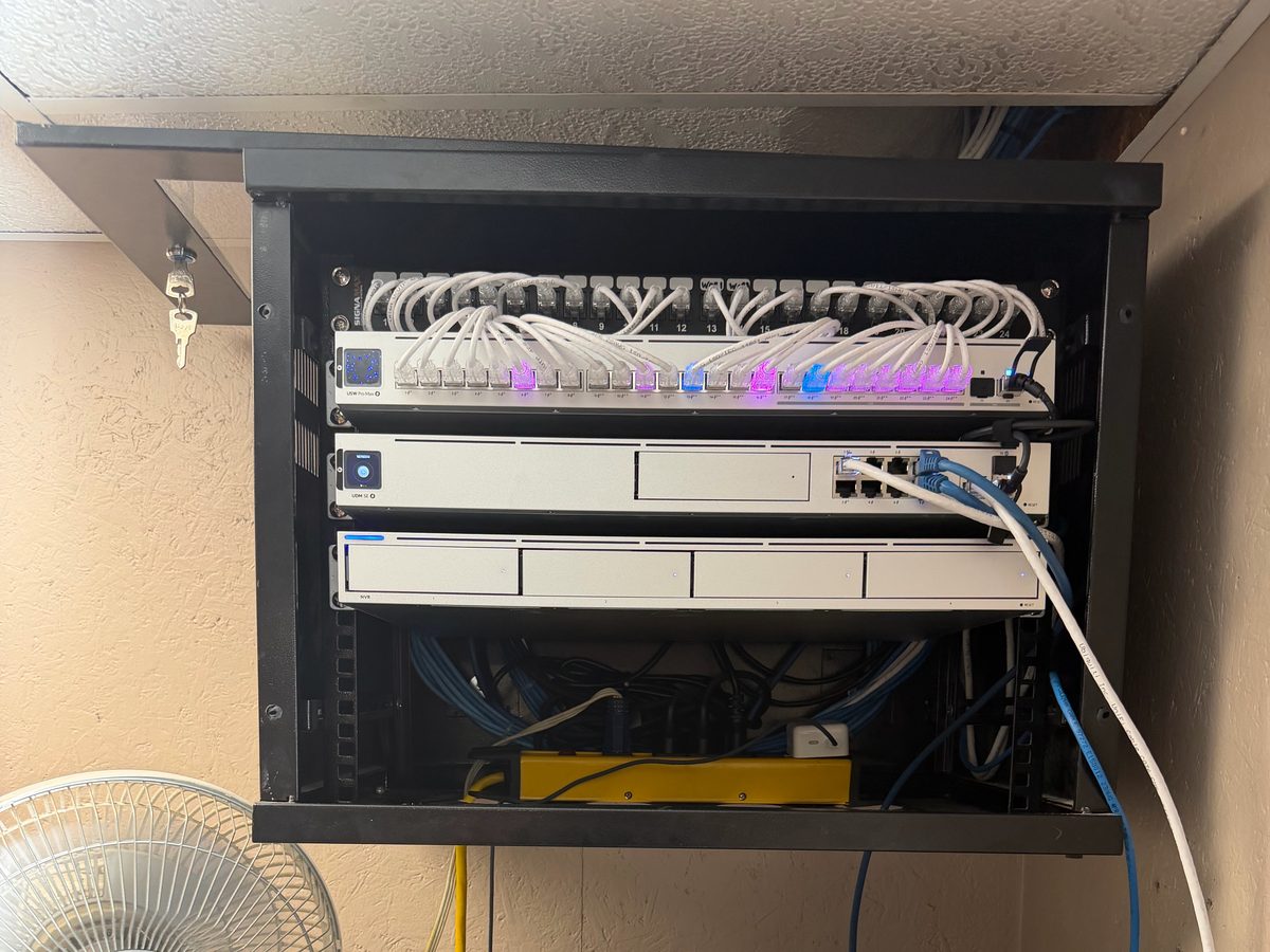 Wall rack with UniFi Dream Machine Pro, UNVR, and PoE switch at an auto body shop
